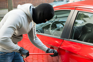 Man demonstrating vehicle theft by breaking into a red car - illustrating the security threat that LostMod GPS trackers help prevent with real-time tracking and anti-theft protection features